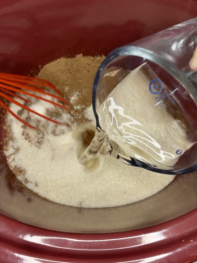 hot water being poured in a slow cooker with sugar and cocoa